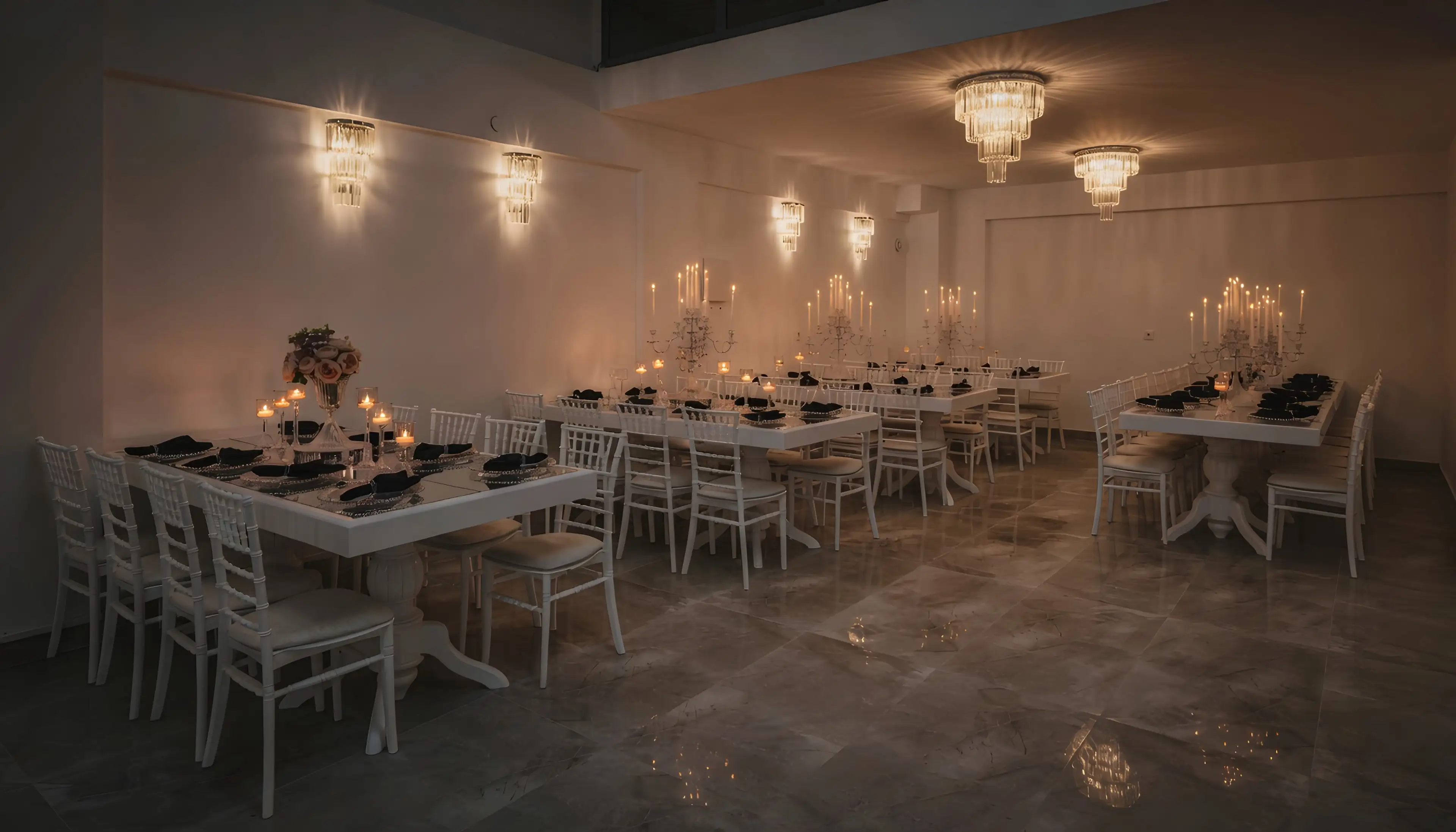 Beyaz masa ve sandalyelerle kurulmuş aydınlık salon, duvarlarda kristal aplikler